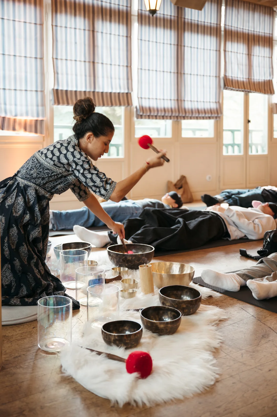 Practitioner walking among reclining participants during an evening sound bath, Résonance studio, Paris 16